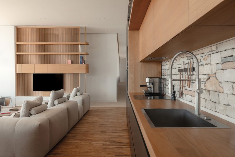 Open-plan kitchen and living area with slatted wood media unit and exposed stone wall backsplash