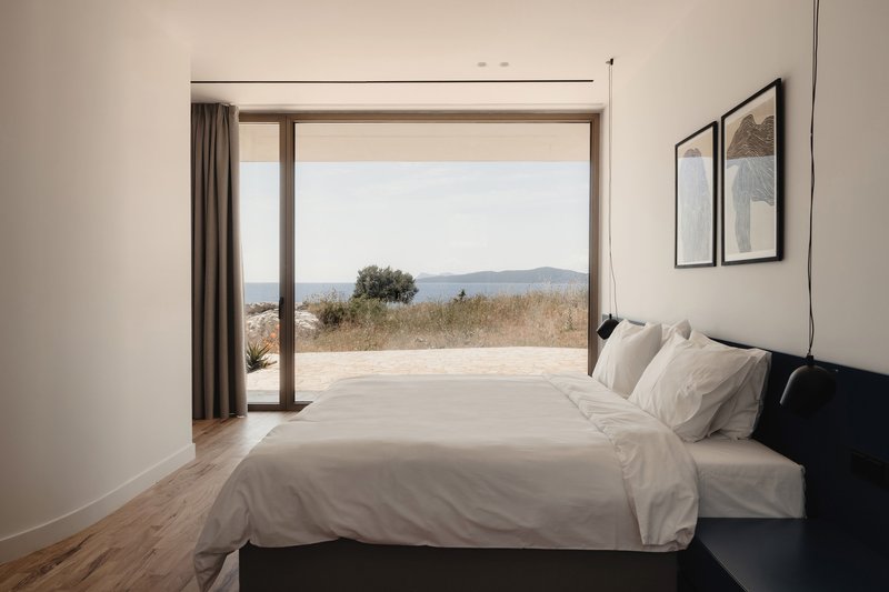 Bedroom with floor-to-ceiling glazing opening onto a terrace overlooking distant hills and coastline