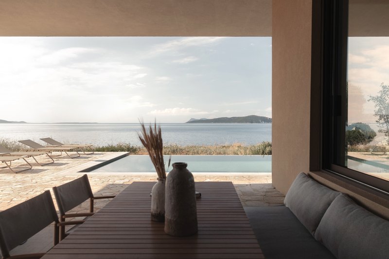 Covered terrace with timber dining table overlooking an infinity pool and distant coastal islands