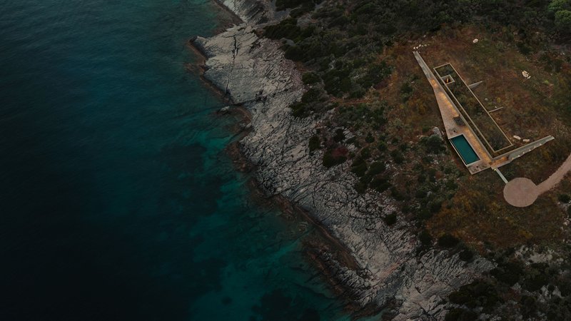 Aerial view of the rectangular pool terrace on a rocky coastal headland with dark blue water
