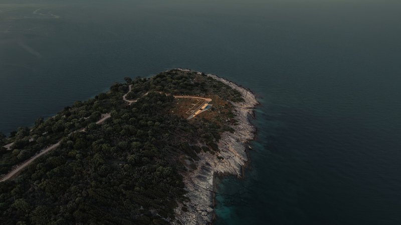 Aerial view of a forested peninsula with a rectangular clearing on its ridge overlooking dark blue water