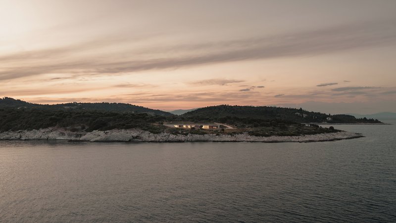 Distant view of a low horizontal structure nestled on a rocky coastline at sunset