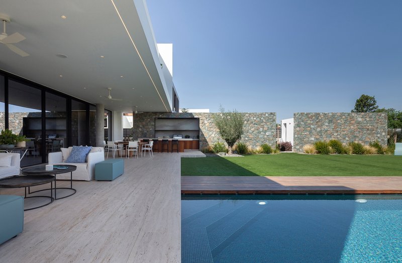 Covered terrace with travertine paving extending from the living area toward the pool and stone boundary wall