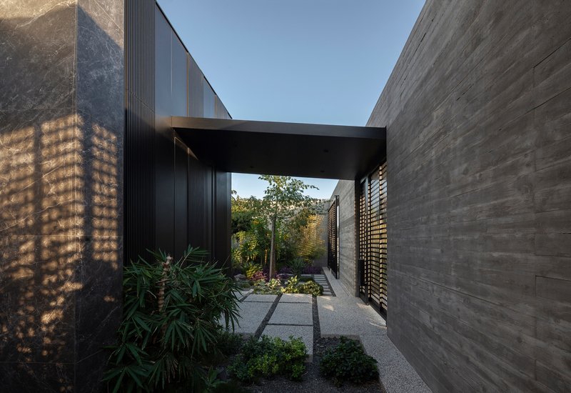 Covered entry passage with perforated stone screen wall and planted courtyard garden under a black beam