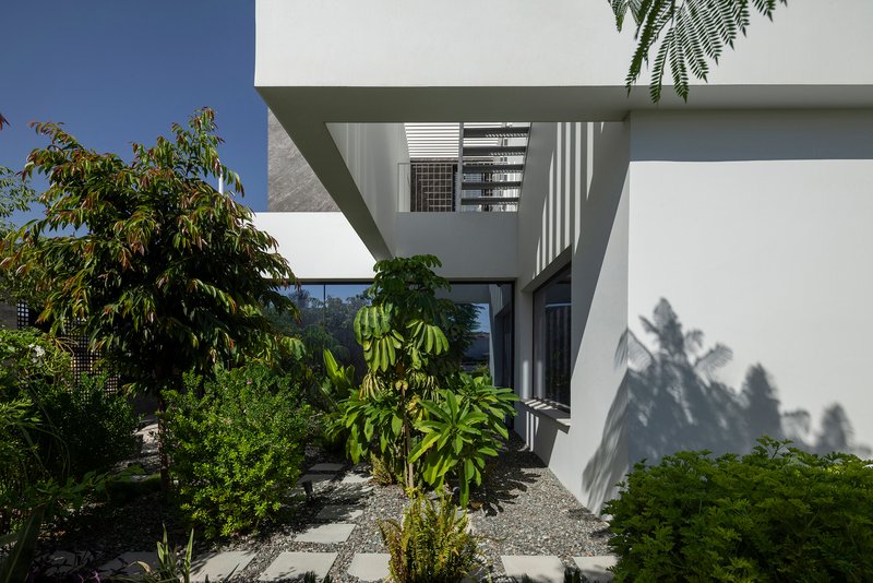 Cantilevered upper volume extending over landscaped courtyard with planted trees and gravel ground surface