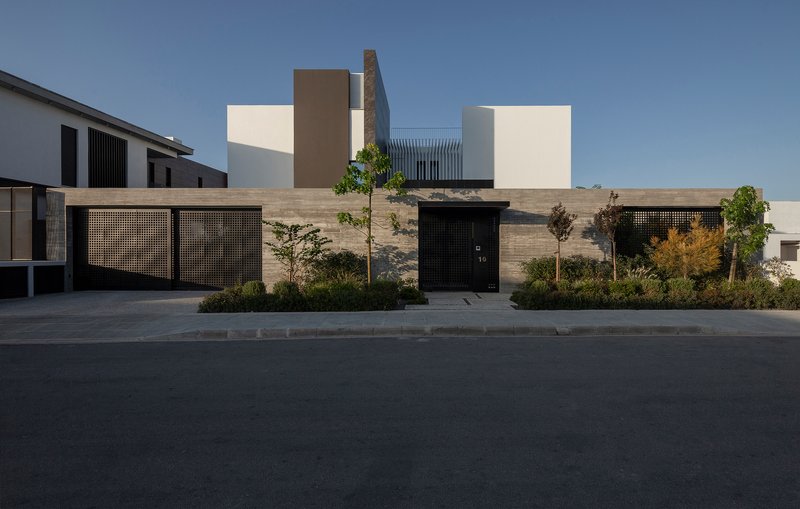 Street view of the perforated metal fence and black entrance door set within a horizontal stone wall