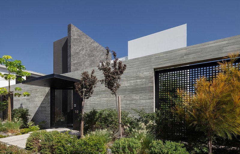 Entrance facade showing horizontal stone cladding and perforated metal screens surrounded by planted shrubs and grasses