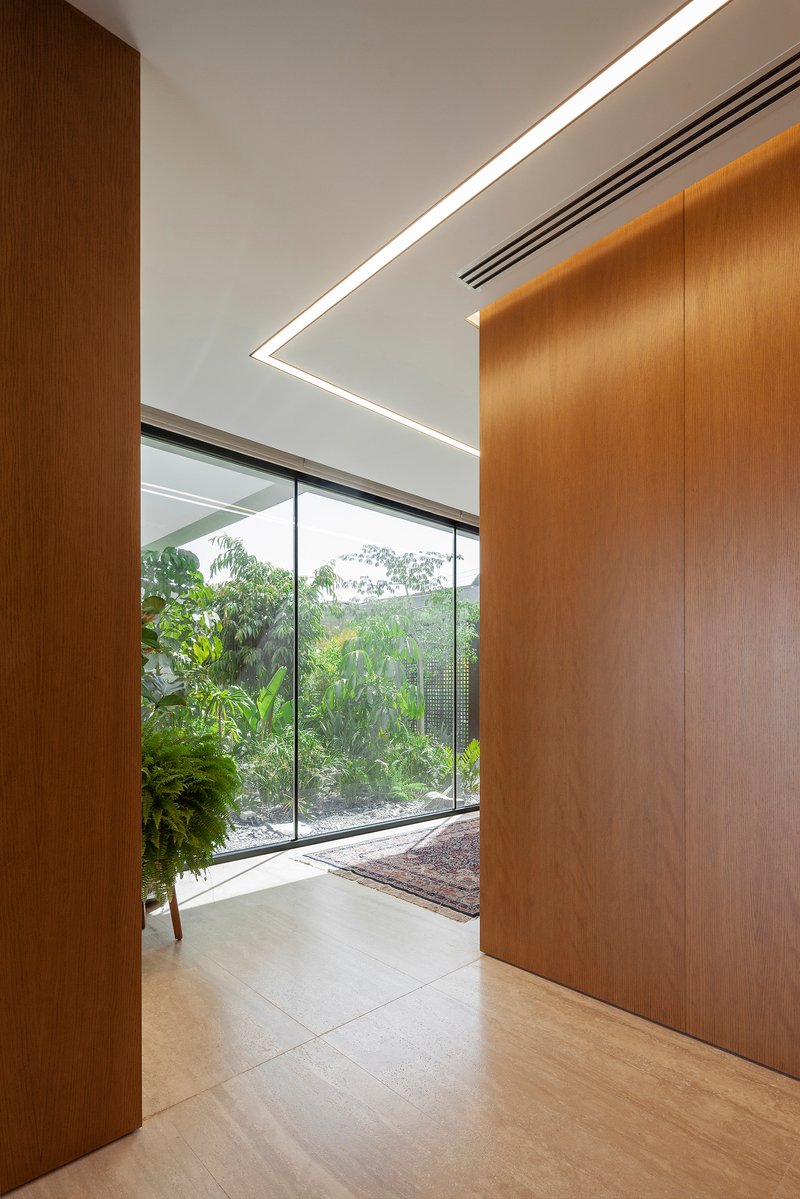 Wood-paneled corridor with angled ceiling light fixture and glazed opening onto garden courtyard