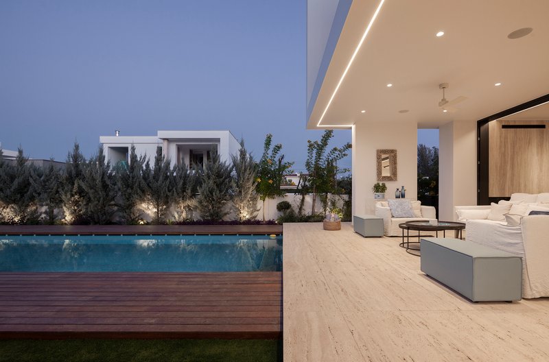 Covered terrace opening to timber deck pool and planted garden at dusk