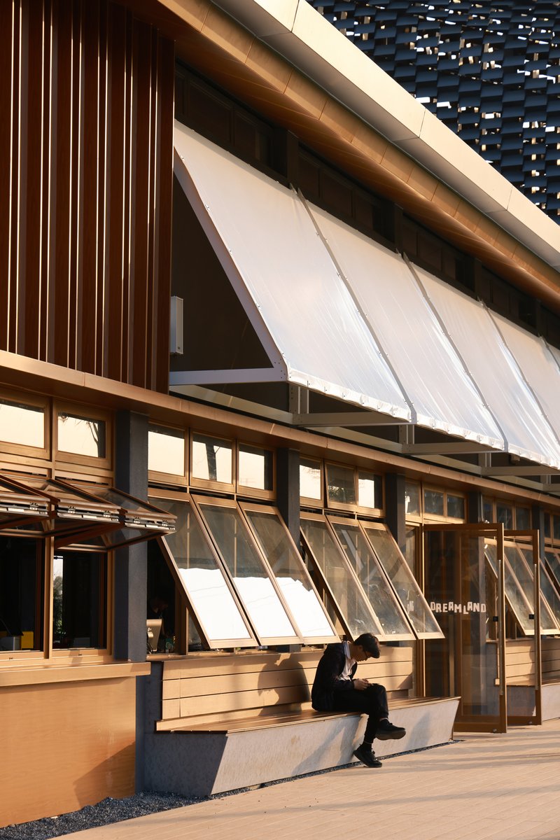 Hinged glazed panels below timber soffits where a person sits on a concrete bench