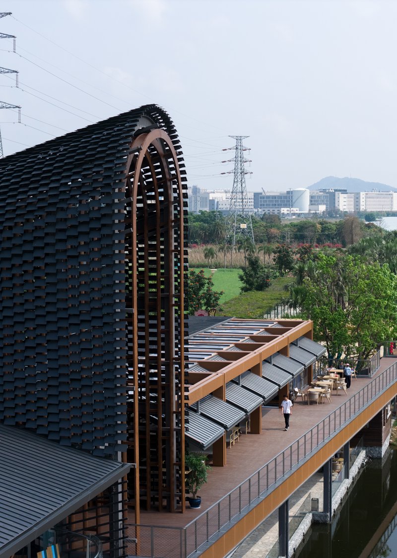 Curved brick tower with perforated arches rising above a timber-framed walkway and water channel