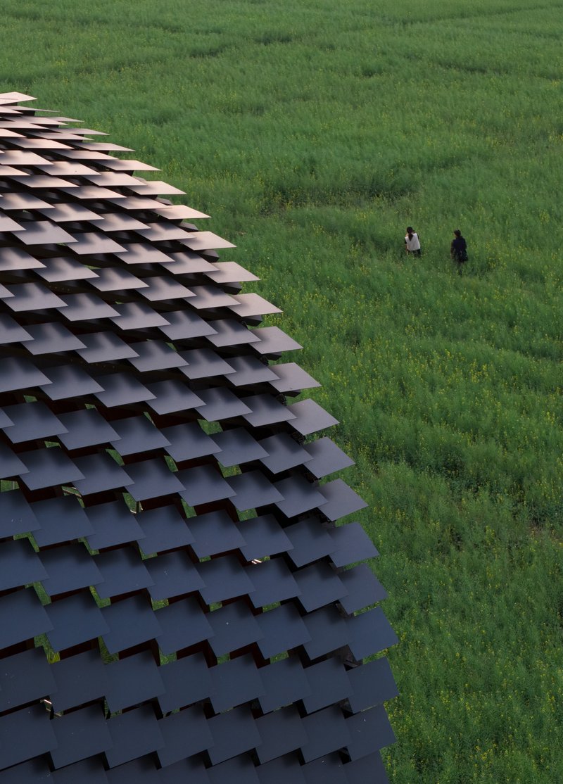 Aerial view of the layered tile canopy edge with two figures standing in the green field