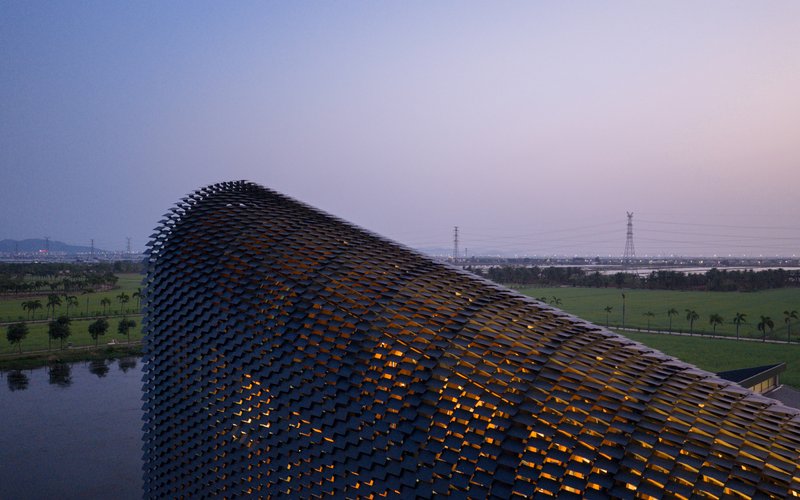 Drone view of the perforated tile roof structure illuminated from within at dusk over rice paddies