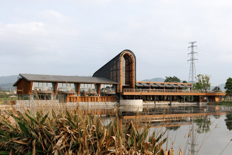 Long view across the reflecting pond showing the arched roof and horizontal timber pavilion with grasses