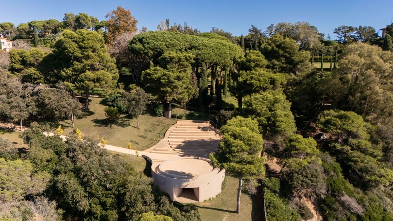 Drone view of curved pavilion with cantilevered roof terrace surrounded by pine trees