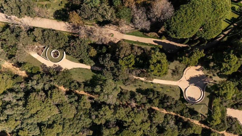 Top-down view of two circular pavilions connected by winding pathways through wooded landscape