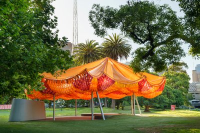 This architectural image showcases a vibrant orange pavilion situated in a lush park setting. The st