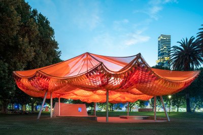 The image showcases a contemporary pavilion in an urban park setting. The structure features a strik