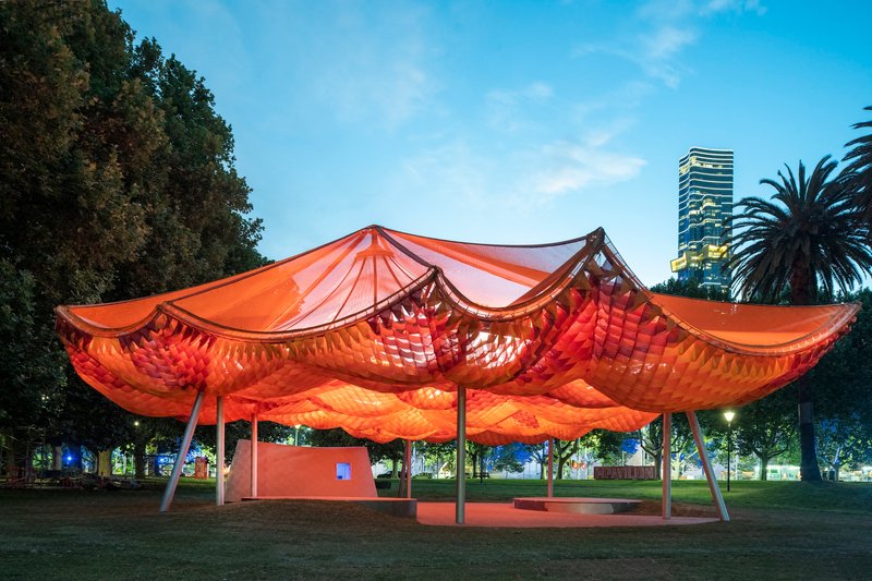 The undulating fabric canopy lit from within at dusk against a darkening sky