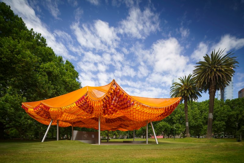 Long view of the tensile canopy structure set in a lawn with palm trees under blue sky