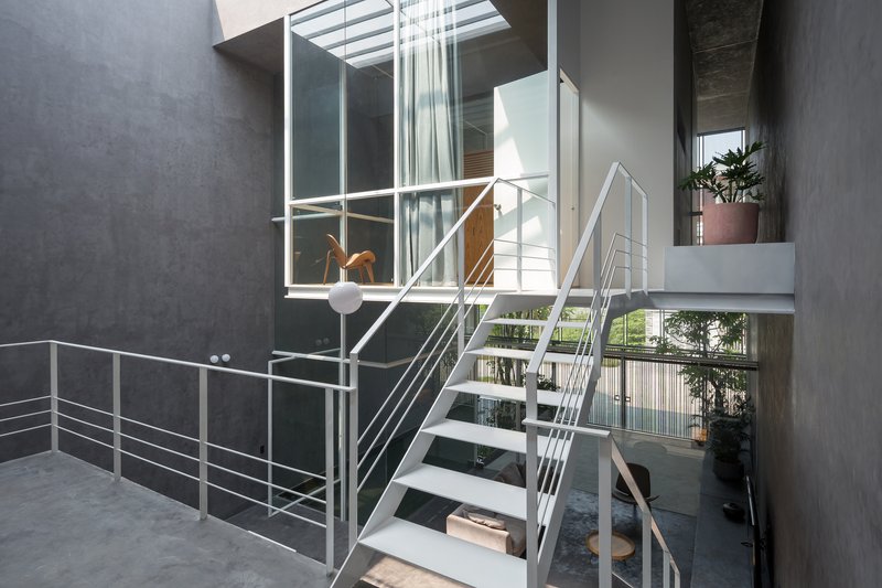 Open-tread steel staircase with cable railings rising through the double-height courtyard space