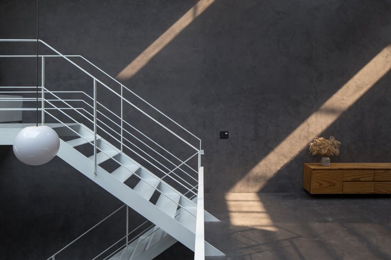 White steel staircase with horizontal cable railings against dark grey wall, with angular sunlight patterns crossing the surface