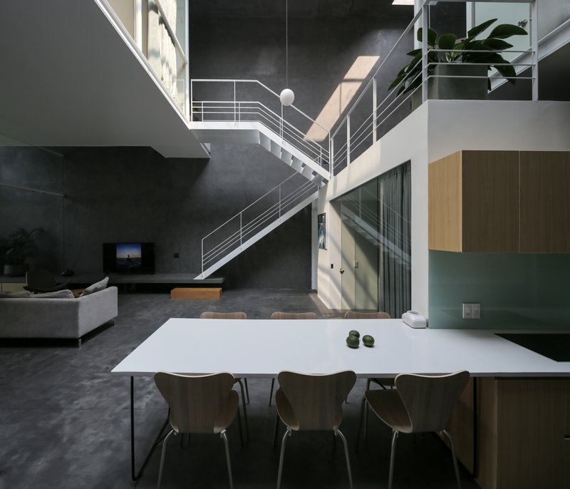 Open-plan dining area with white table beneath steel staircase and double-height concrete walls