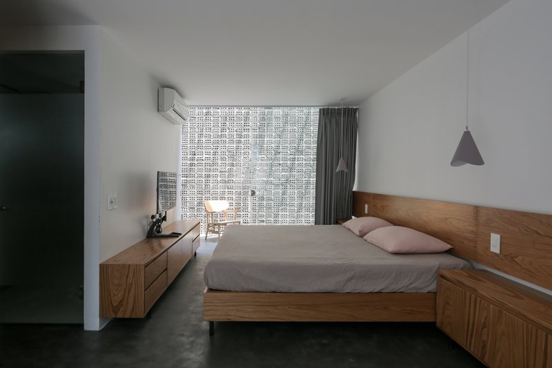 Bedroom with timber platform bed, low credenza, and perforated screen wall filtering daylight through grey curtains