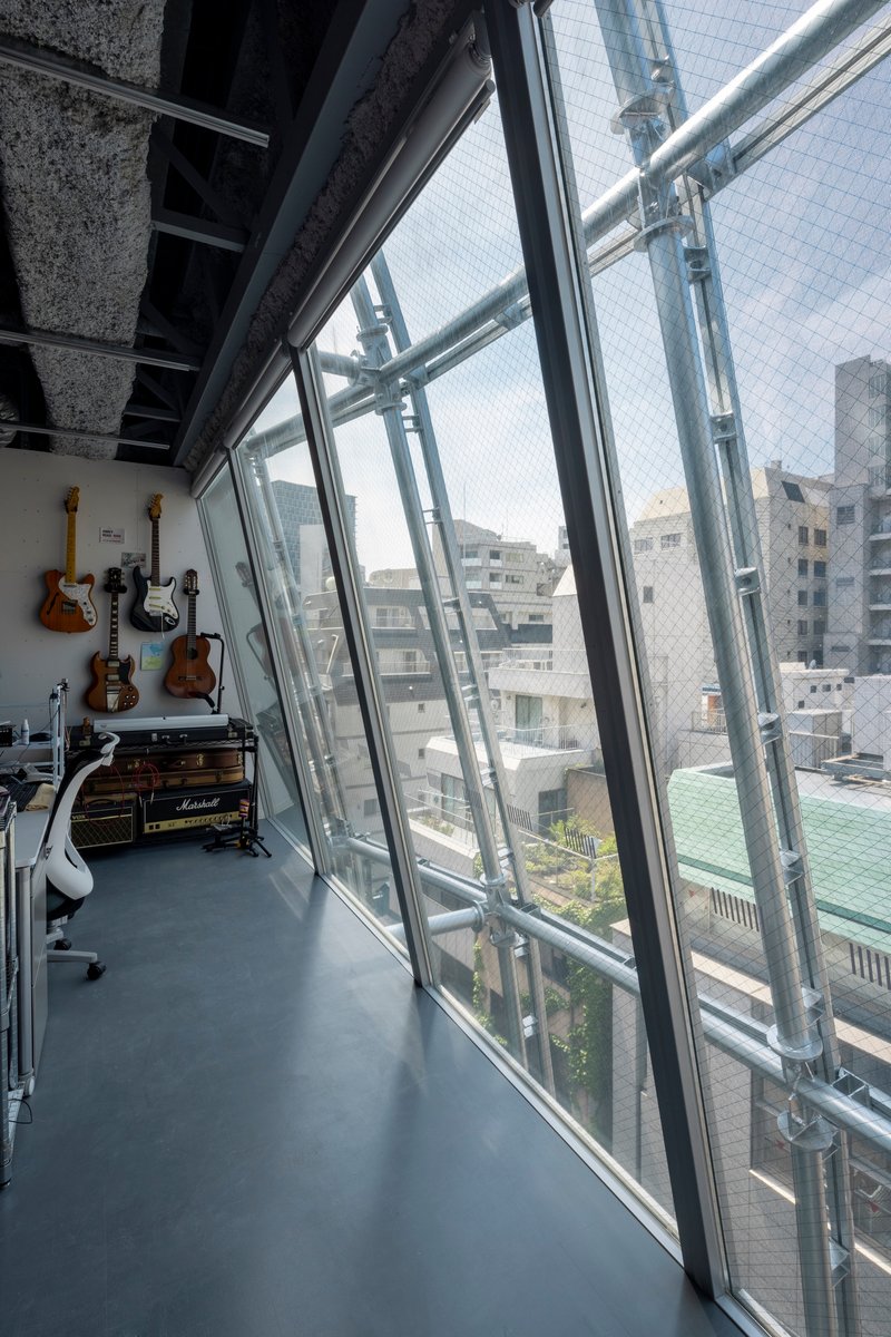 Angled glass curtain wall with visible steel bracing and guitars mounted on the interior wall
