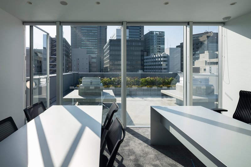 Glazed office space opening to a rooftop terrace with planters and high-rise buildings beyond