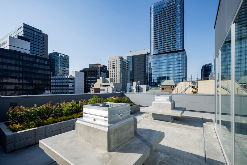 Rooftop terrace with concrete planters, raised garden beds, and stepped seating under clear blue sky