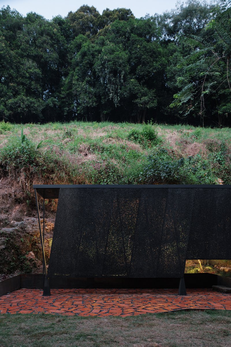 Freestanding perforated black screen wall on a herringbone brick terrace facing an overgrown hillside