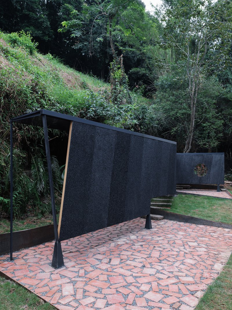 Angular screen wall with angled support struts on a patterned brick terrace backed by forested slope