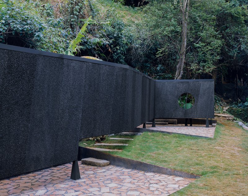Paired curving black walls with circular aperture creating courtyard spaces connected by patterned stone paving