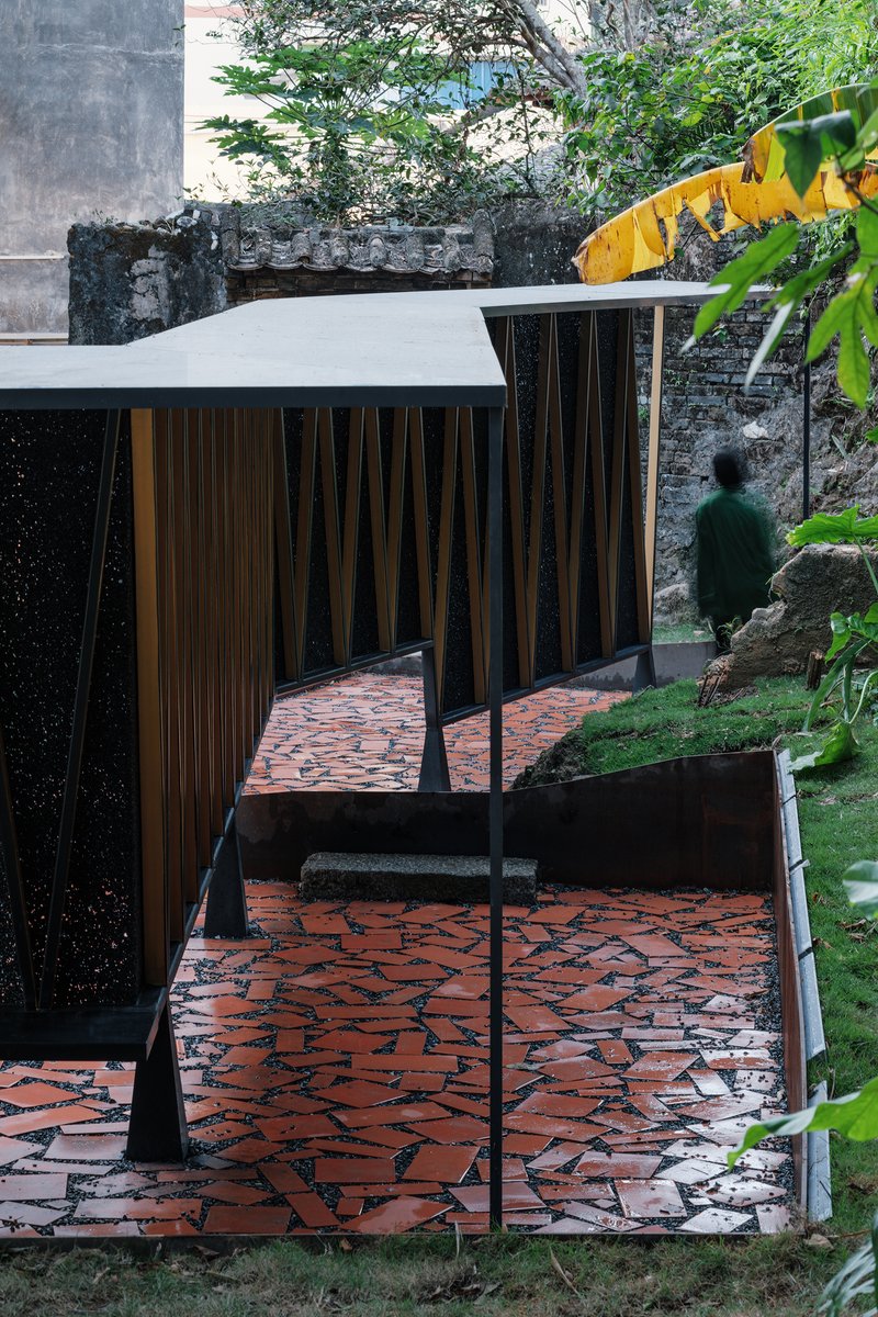 Pavilion interior with timber slat walls and white roof canopy seen from red terracotta paved terrace