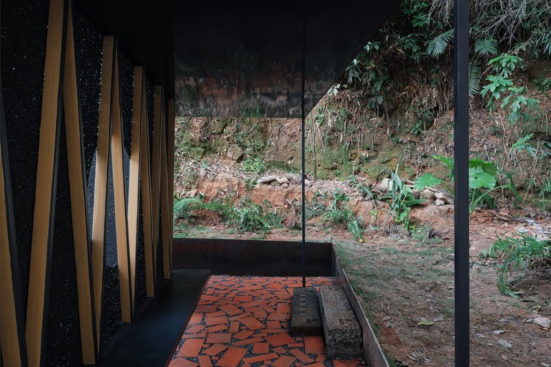 Interior view through timber slat screen toward hillside with vegetation and fallen leaves