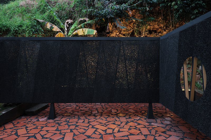 Covered terrace with red mosaic floor and black terrazzo walls with circular openings framing foliage