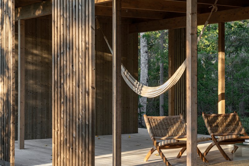 Vertical timber slat screen framing a hammock and folding chairs on an open porch at dusk