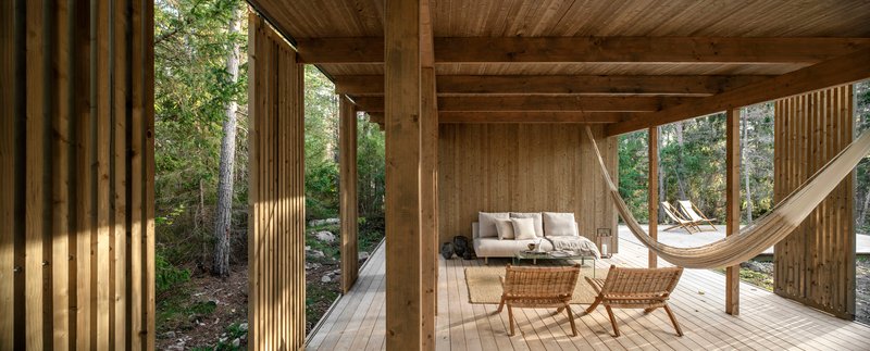 Covered porch with timber columns, plank ceiling and hammock opening to the forest