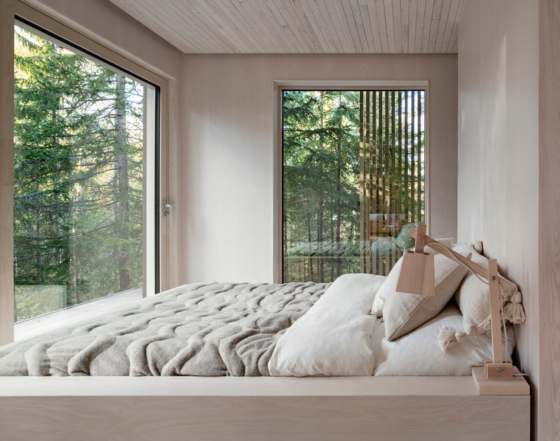 Bedroom with timber platform bed and floor-to-ceiling windows framing views of surrounding pine forest