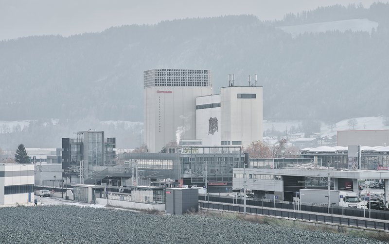 Industrial complex with concrete tower and perforated parapet set against misty forested hills in winter
