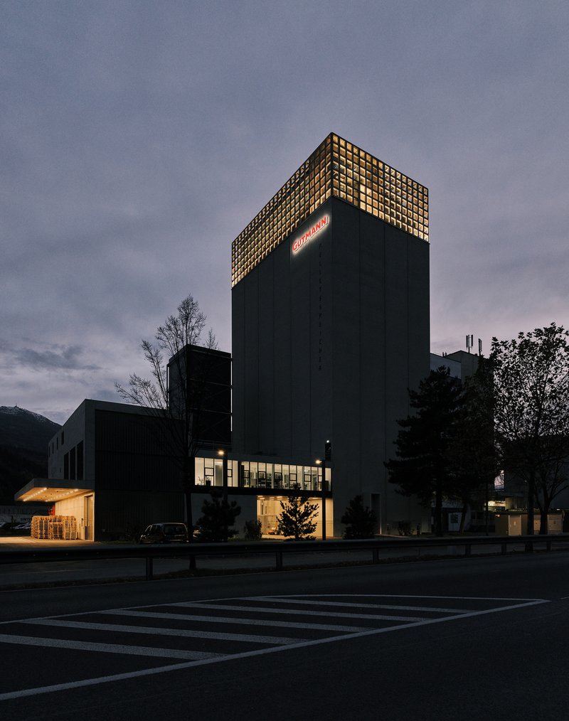 Nighttime view of the illuminated concrete tower with glowing perforated crown and lit ground floor openings