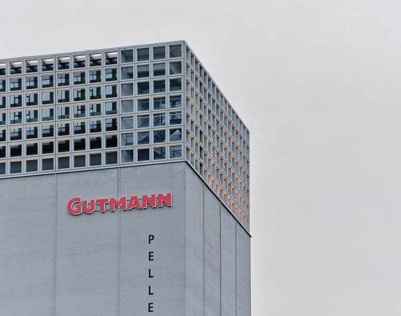 Corner view of the concrete podium and gridded glass facade above under an overcast sky