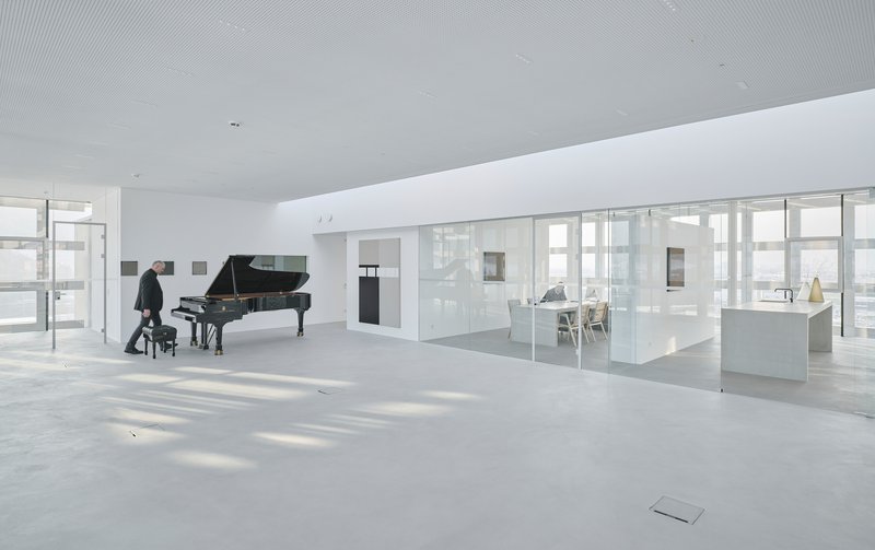 White terrazzo floor and glass-walled room with a person seated at the piano by the windows