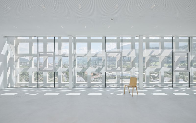 Single wooden chair facing the perforated white screen wall and full-height glazing beyond