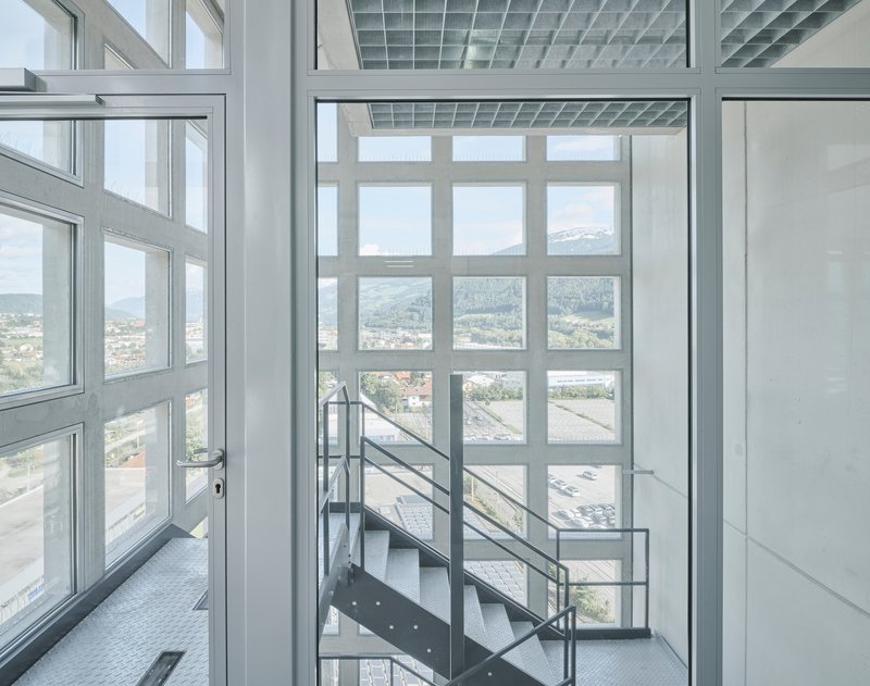 Steel staircase with wire mesh railing rising through a white-framed glass curtain wall overlooking distant mountains
