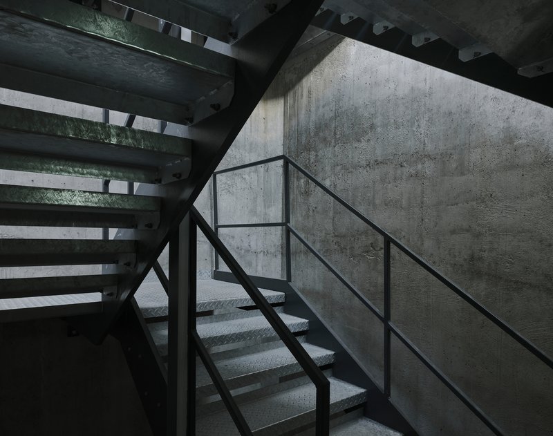 Metal staircase with perforated treads against board-formed concrete wall in shadowed stairwell
