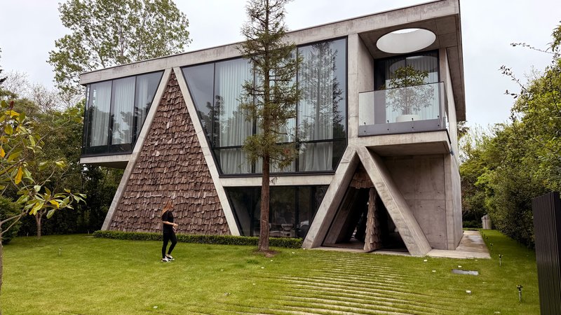 Side view of the triangular textured volume and diagonal concrete supports with a person walking on lawn