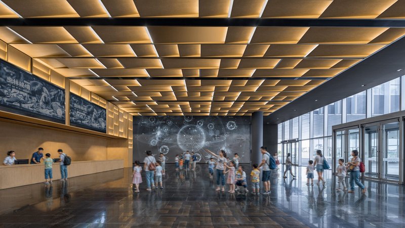 Entry lobby with coffered timber ceiling and visitors gathered before a projection wall
