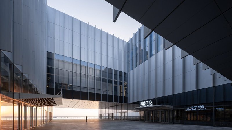 Covered plaza between translucent ribbed facades and illuminated timber soffit at twilight